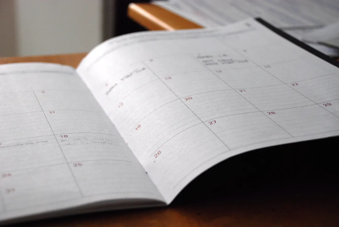 Oppslått månedskalender i en papirplanlegger på et trebord, med datoruter i fokus og sidene som bøyer seg